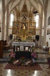 Kirchenraum mit goldenem Hochaltar, davor Blumenschmuck