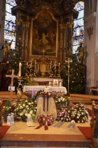 Kirchenraum mit Barockaltar und Altarbild, davor Blumenschmuck
