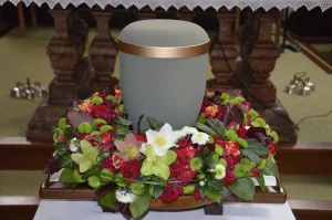 Graue Urne auf einem Blumenbett aus roten und weißen Blüten
