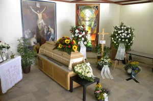 Aufbahrungsraum mit Kreuzbild, Sarg und Blumenschmuck aus Sonnenblumen
