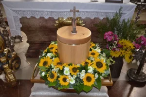 Helle Holzurne mit Kreuz, umgeben von einem Kranz aus Sonnenblumen
