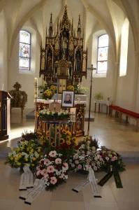 Kirchenraum mit neugotischem Altar, davor Blumenschmuck