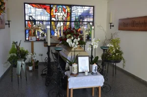 Aufbahrungsraum mit Buntglasfenster, Blumenschmuck und Kerzen