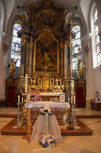 Kirchenraum mit Barockaltar und Altarbild, davor Blumenschmuck