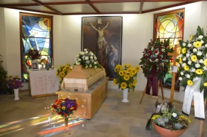 Aufbahrungsraum mit Kreuzbild, Sarg und Blumenschmuck mit Sonnenblumen
