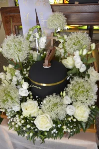 Schwarze Urne mit Goldrand in einem Kranz aus weißen Rosen und Allium