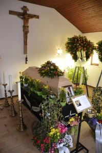 Aufbahrungsraum mit Kruzifix, Sarg und reichem Blumenschmuck