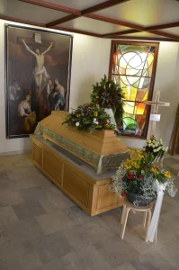 Aufbahrungsraum mit Kreuzbild und Buntglasfenster, Sarg mit Blumenschmuck