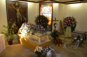 Aufbahrungsraum mit Kreuzbild, Sarg mit weißem Blumenschmuck