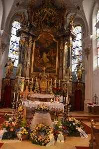 Kirchenraum mit goldenem Barockaltar, davor Blumenschmuck