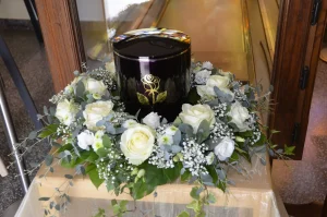 Schwarze Urne mit Goldrand in einem Kranz aus weißen Rosen und Eukalyptus